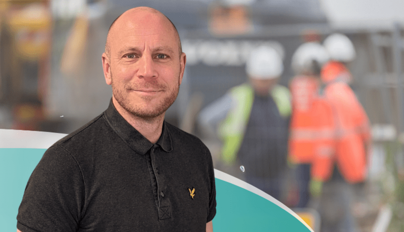  A man in a black polo shirt in front of blurred picture of construction workers