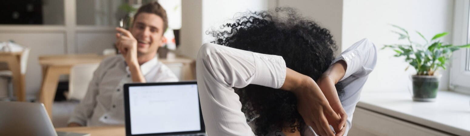 A woman leaning back talking with a colleague in front of her desk