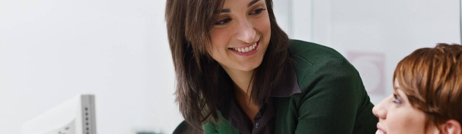 A woman smiling standing over the shoulder of her human resources colleague