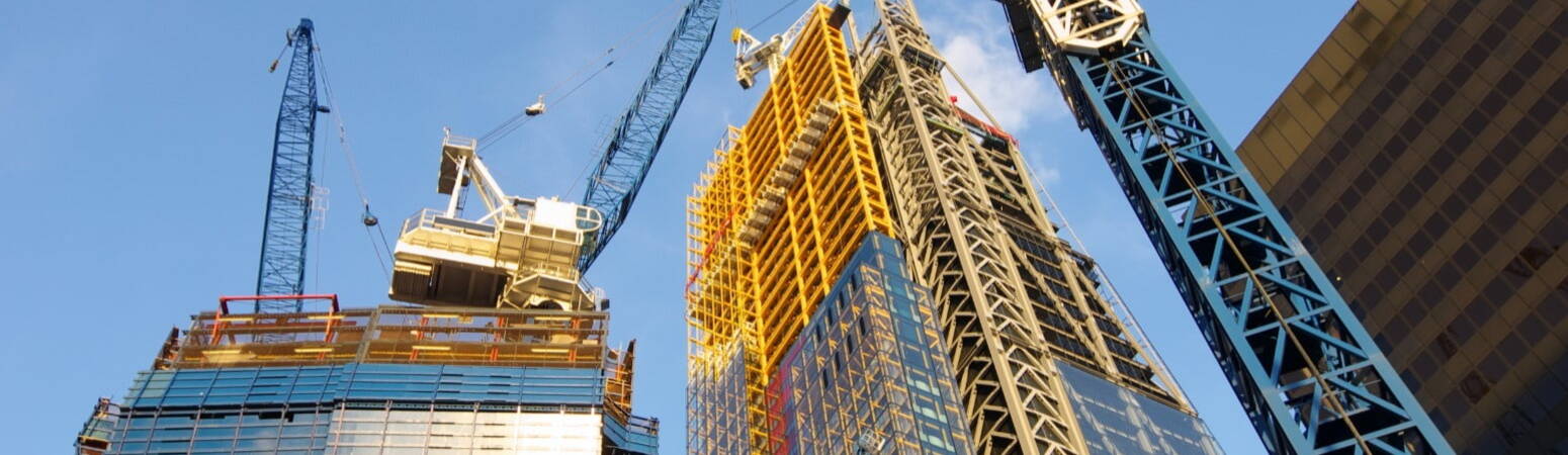 Looking up at the construction of a new building with cranes beside it